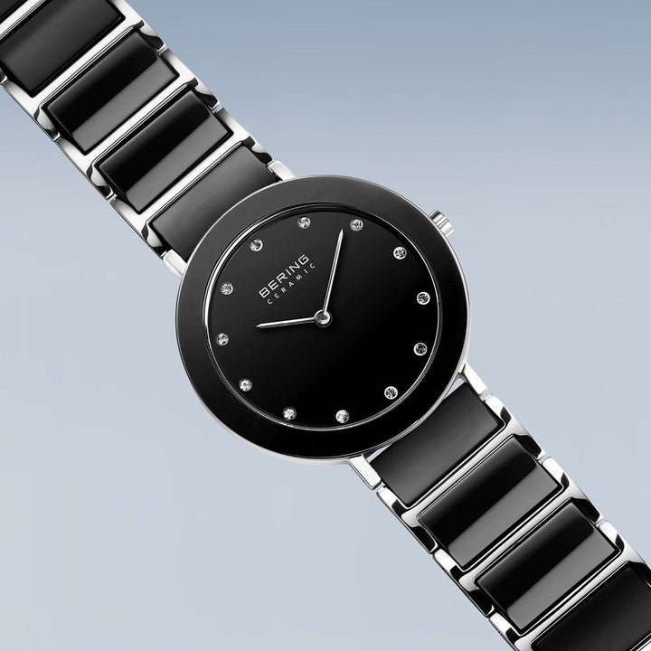 De 11435-749 van Bering is een strak zwart keramisch horloge met een quartz uurwerk en ronde wijzerplaat. Het heeft minimalistische uurmarkeringen, de merknaam, een gepolijste metalen schakelband en stevig saffierglas tegen een zachte blauwgrijze gradiënt.