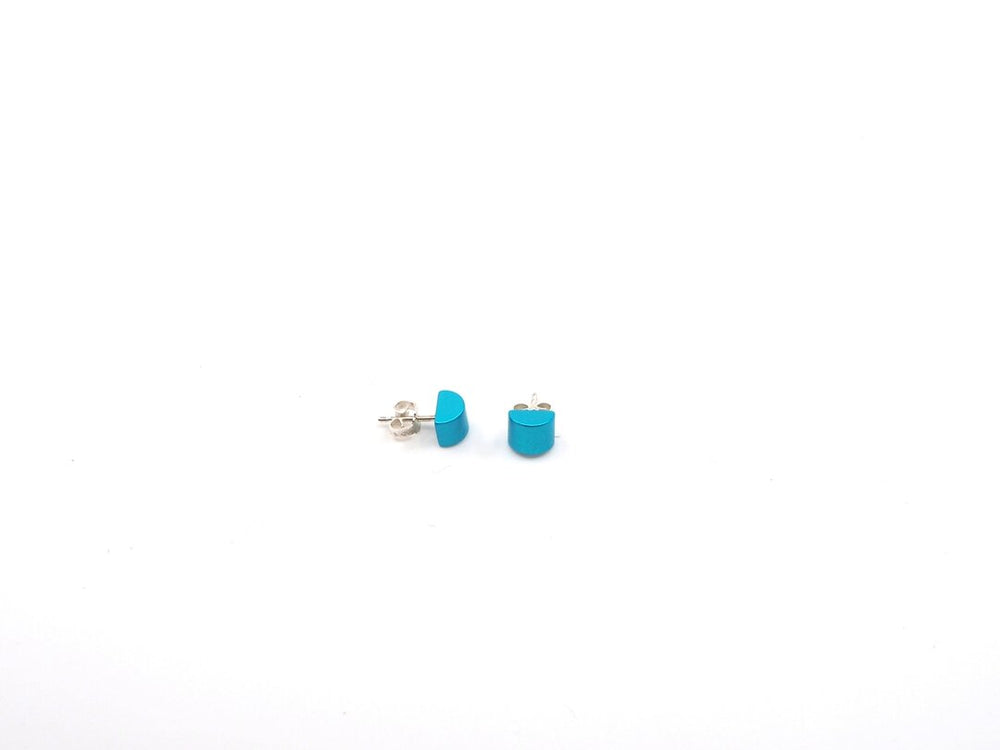 Twee turquoise Gekleurde kubus oorbellen van Otra Cosa, met zilveren achterkant, zijn geplaatst op een effen witte achtergrond.