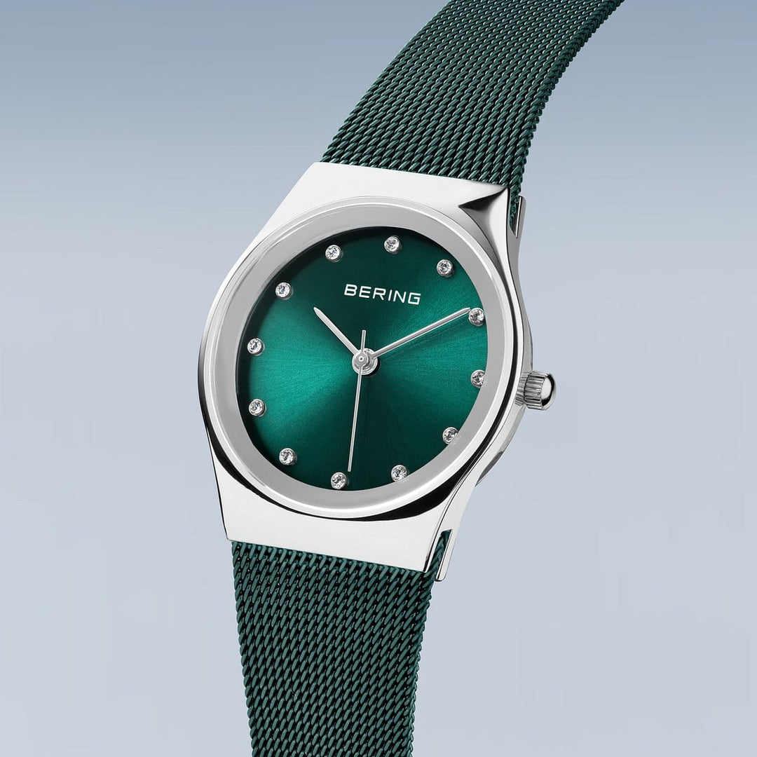 Het Bering 12927-808 horloge heeft een zilveren kast met een metallic groene wijzerplaat en Milanees bandje. Het beschikt over een nauwkeurig quartz uurwerk, zilveren edelsteenachtige uurmarkeringen en wijzers, plus het elegante Bering logo op een lichte gradiënt achtergrond.