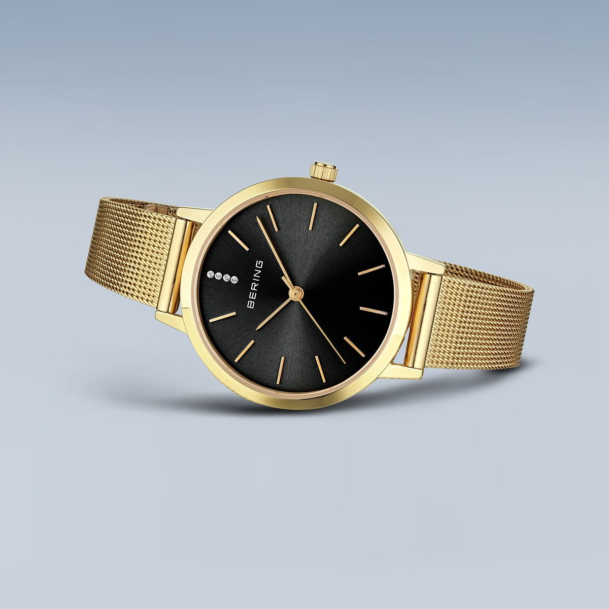 De Bering dames horloge zwarte wijzerplaat 13434-332 heeft een goudkleurige Milanees band, zwart minimalistisch wijzerplaat, gouden markers en saffierglas, stijlvol getoond tegen een gradiënt lichtblauwe achtergrond.