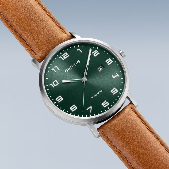 De Bering herenhorloge 18640-568 heeft een groene wijzerplaat met witte cijfers, een titanium horlogekast en een bruine leren band. Het geeft de datum weer, met BERING en TITANIUM elegant gedrukt om het verfijnde ontwerp te benadrukken.