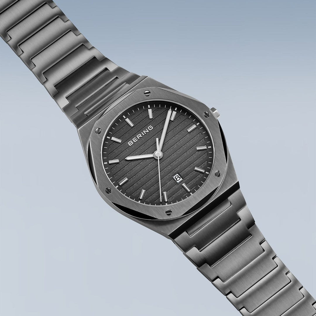 Het Bering Herrenhorloge 19742-777 heeft een roestvrijstalen band en kast, zilveren wijzers, uurmarkeringen, een datumaanduiding op 6 uur en een gestreepte donkergrijze wijzerplaat op een lichtblauwe achtergrond met duurzaam saffierglas.
