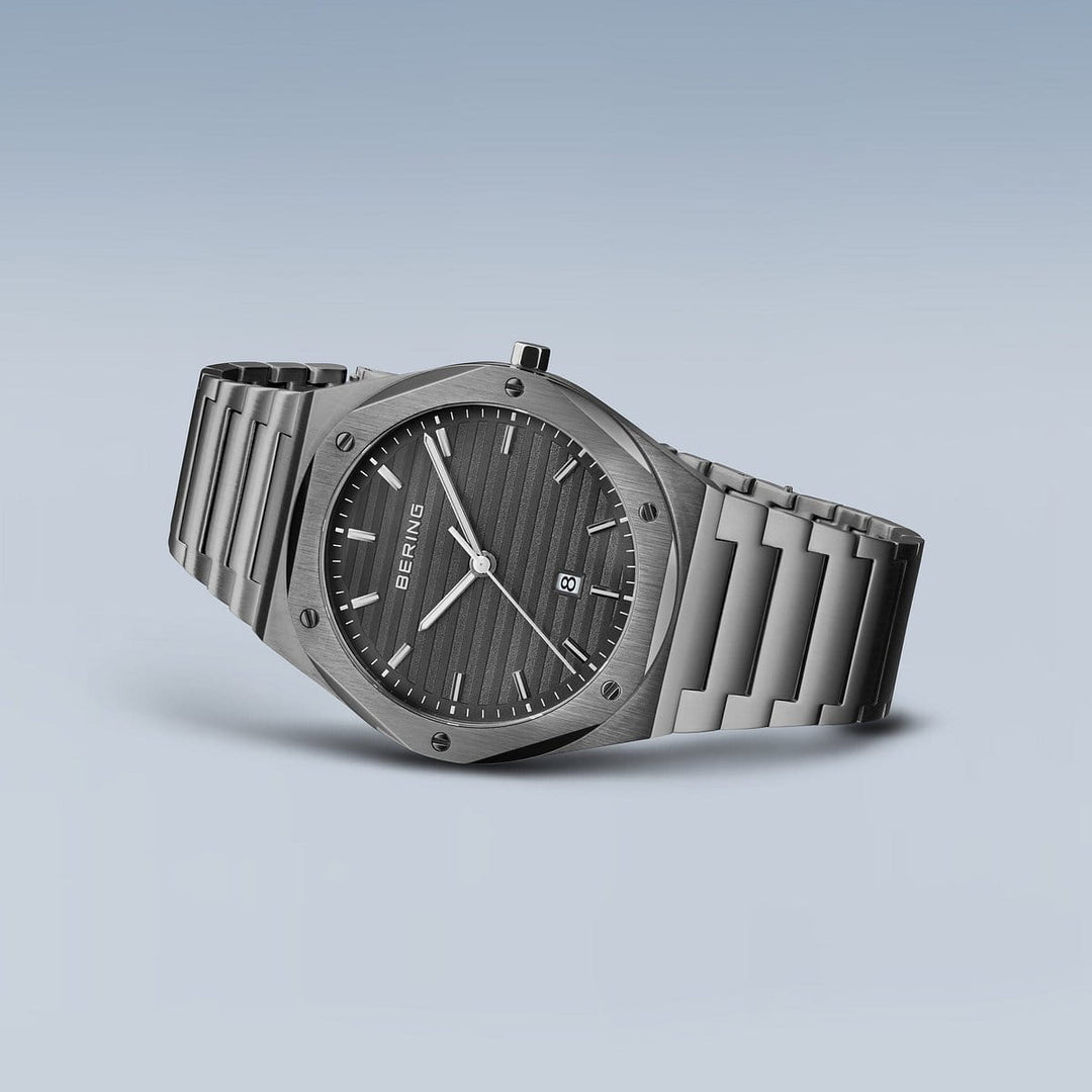 Het Bering herenhorloge 19742-777, met een strakke roestvrijstalen kast en metalen band, benadrukt het minimalistische ontwerp met een zwarte gestructureerde wijzerplaat, zilveren uurmarkeringen, twee zilveren wijzers en een datumaanduiding op een grijze achtergrond met duurzaam saffierglas.