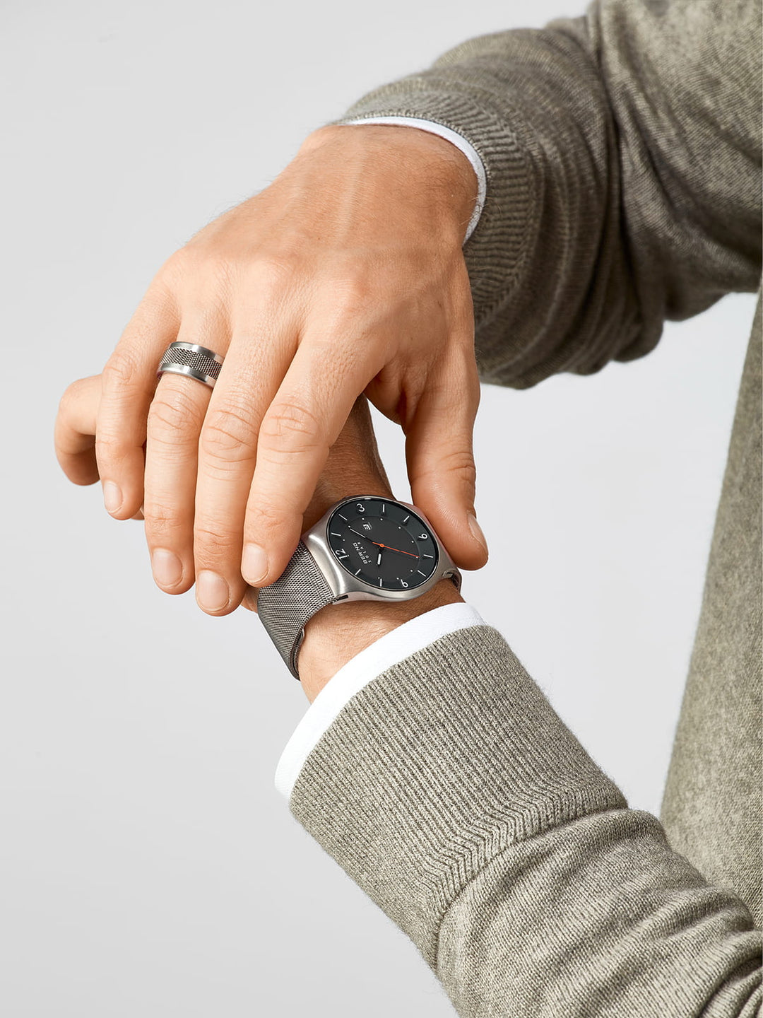 Een persoon in een grijze trui past een Bering-horloge (14440-077) aan met Saffierglas, een zwarte wijzerplaat en Solar-technologie op zijn linkerpols. Een zilveren ring siert de rechterhand tegen een witte achtergrond.