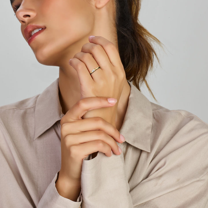 Een vrouw in een beige blouse raakt zachtjes haar nek aan en toont de Van der Kooij Collectie ring met zirkonia 14K geelgoud aan haar vinger. Haar bruine haar is naar achteren gebonden en een effen lichte achtergrond accentueert de elegante ring.