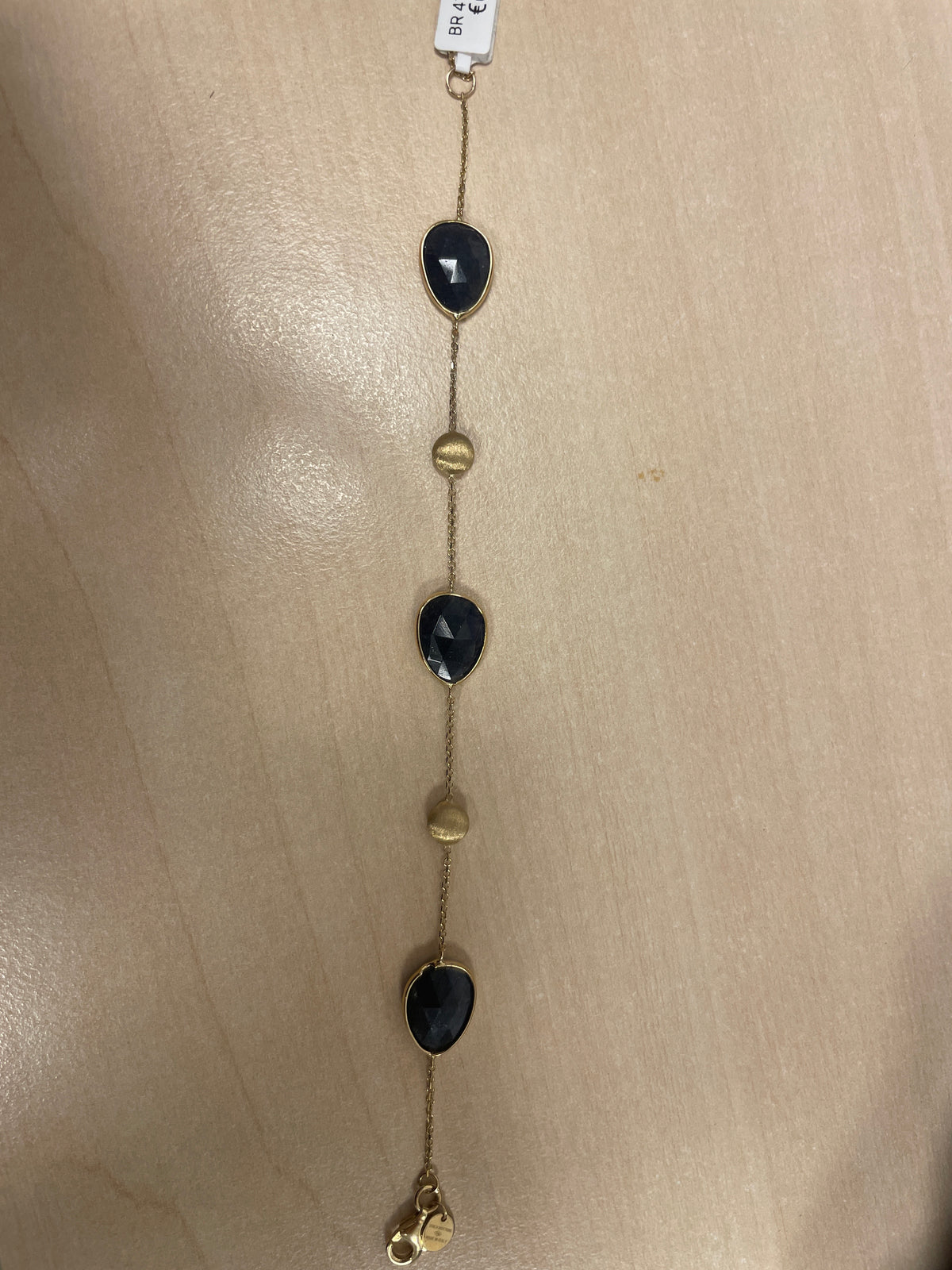 Bracciale in oro con pietre nere e dettagli dorati, design sottile e moderno.