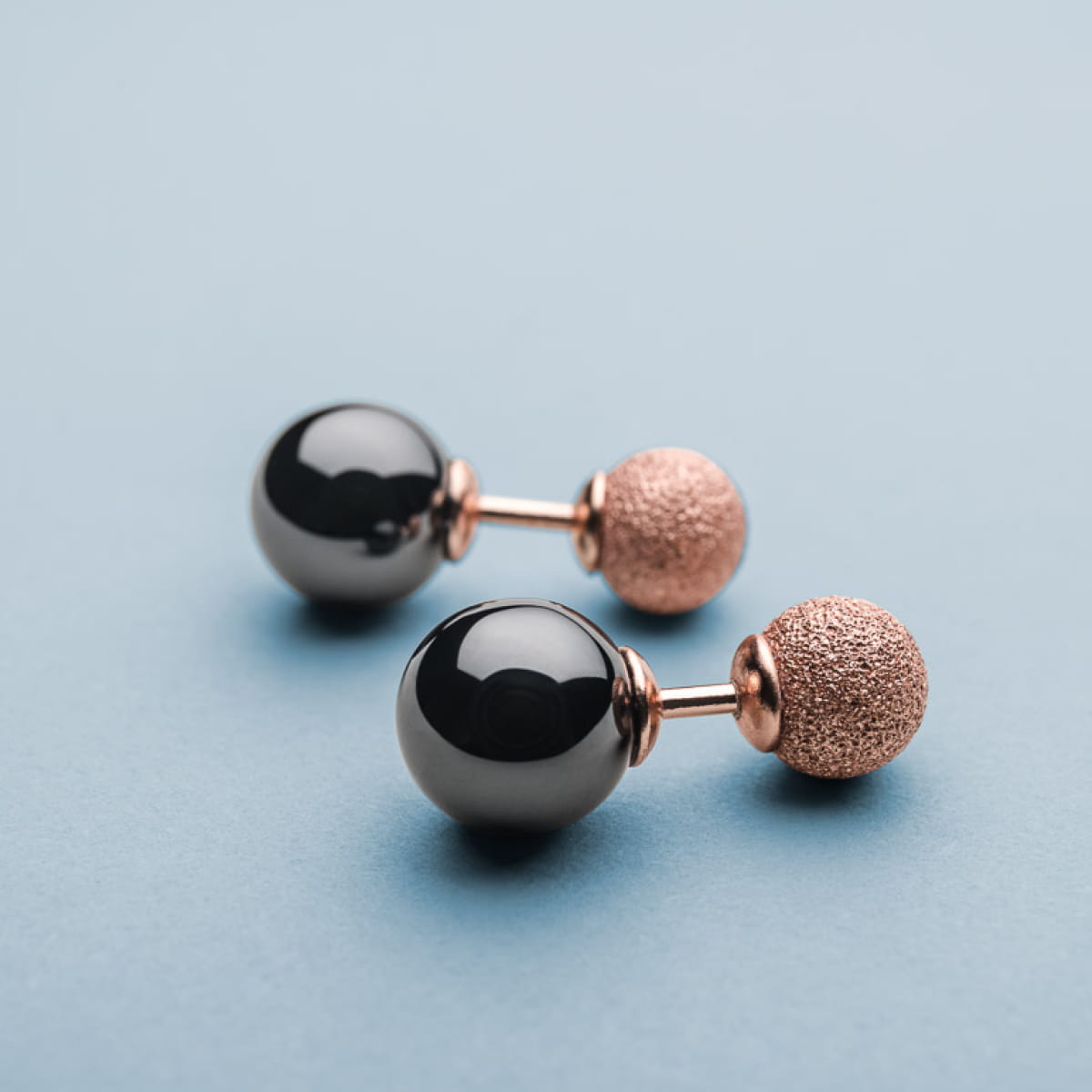 Orecchini con perle nere lucide e dettagli in metallo rosa opaco.