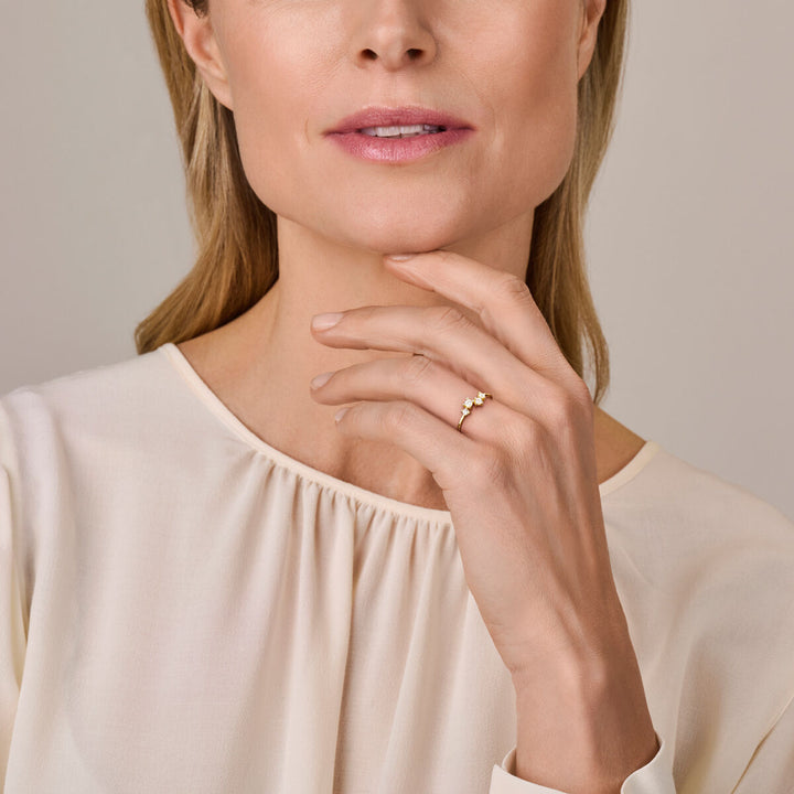 Een vrouw in een crèmekleurige blouse raakt zachtjes haar kin aan en laat de Van der Kooij Collectie ring zirkonia 14K geelgoud aan haar vinger zien. Alleen de onderste helft van haar gezicht en bovenlichaam zijn zichtbaar.