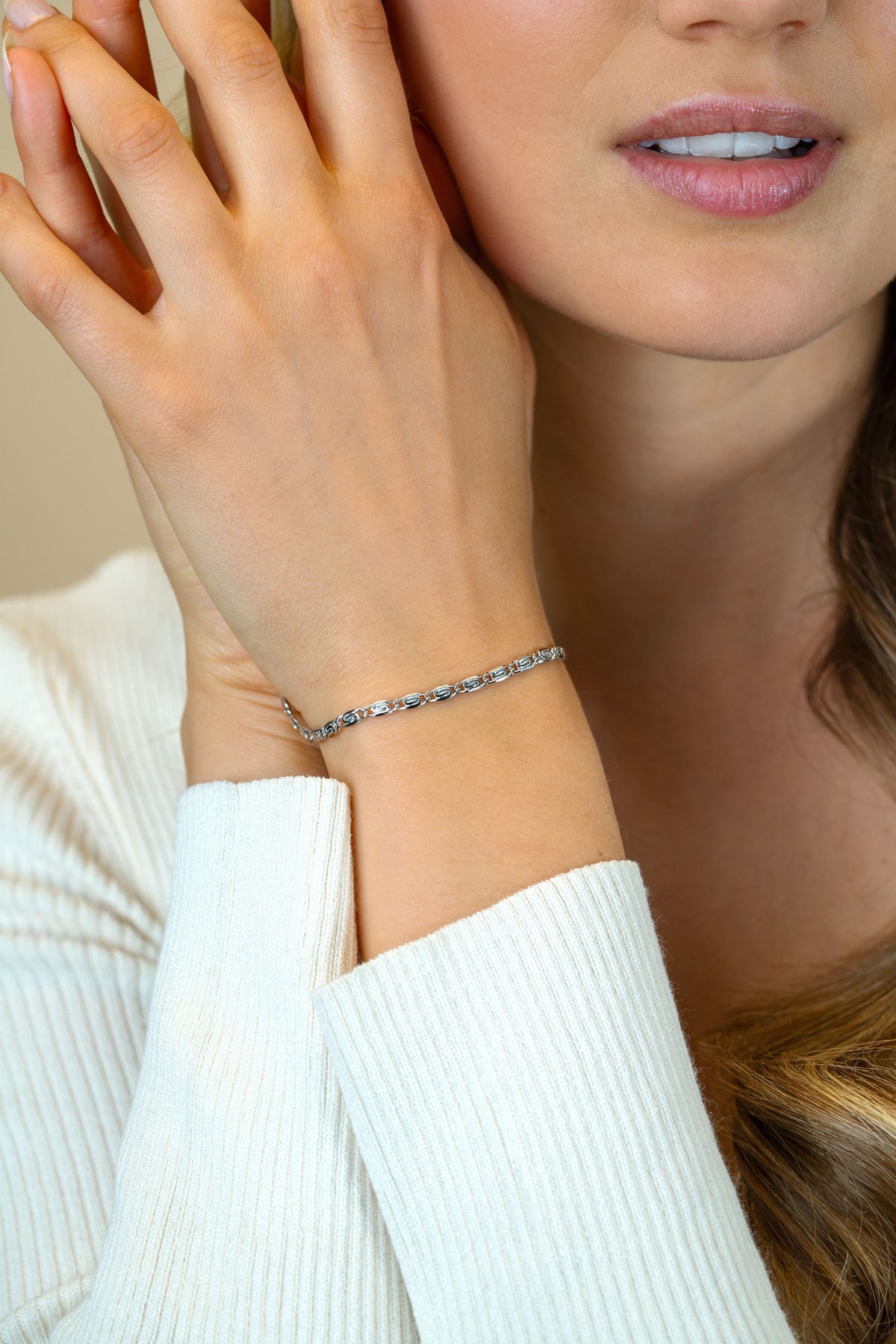 Een vrouw in een witte geribbelde top raakt zachtjes haar gezicht aan, waardoor de Zinzi Armband zilver ZIA2712 met fonkelende steentjes om haar pols wordt benadrukt. Alleen de onderste helft van haar gezicht en de elegante armband zijn zichtbaar.