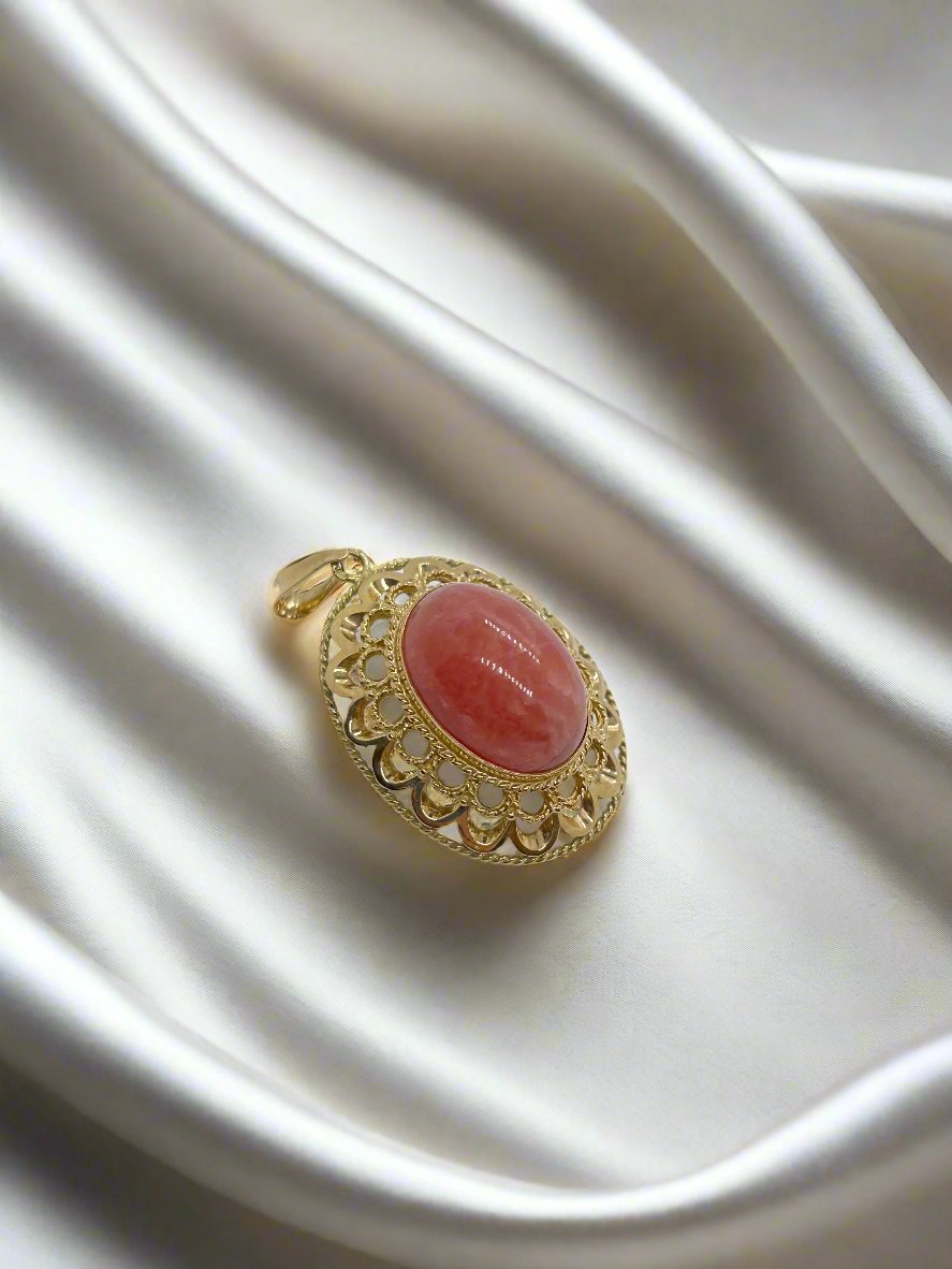 De vintage gouden Hanger 14k rhodochrosiet 8.3gr van Juwelier van der Kooij straalt met zijn ingewikkelde ontwerp en grote ovale rode rhodochrosiet charme uit terwijl hij elegant rust op een luxueuze witte satijnen stof.
