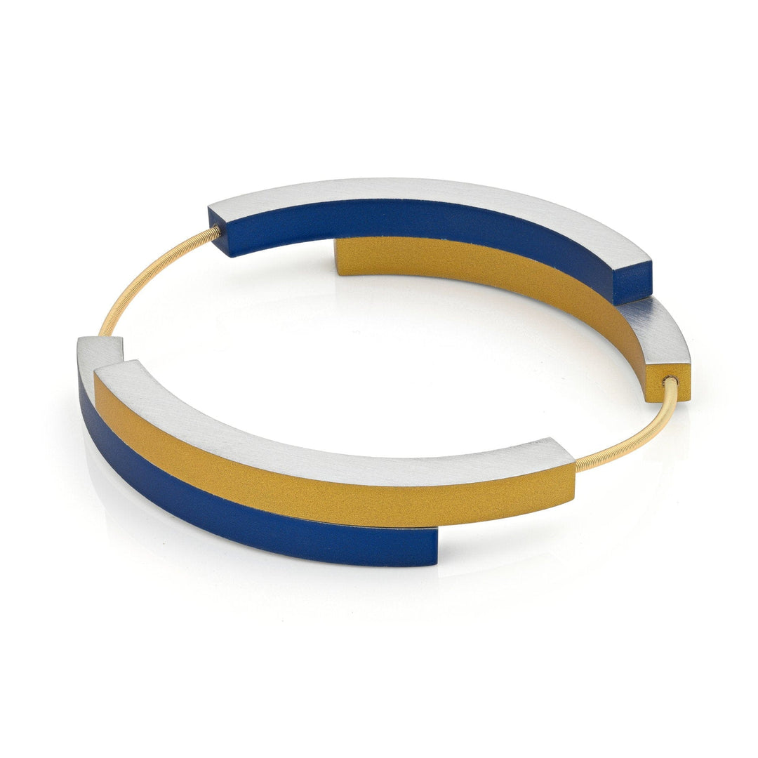 De Armband Vier bogen Blauw Goudkleurig AG32BG van CLIC Creations is een moderne, geometrische armband met zilveren, blauwe en gouden gebogen segmenten verbonden door fijne gouden draden, handgemaakt in Nederland.