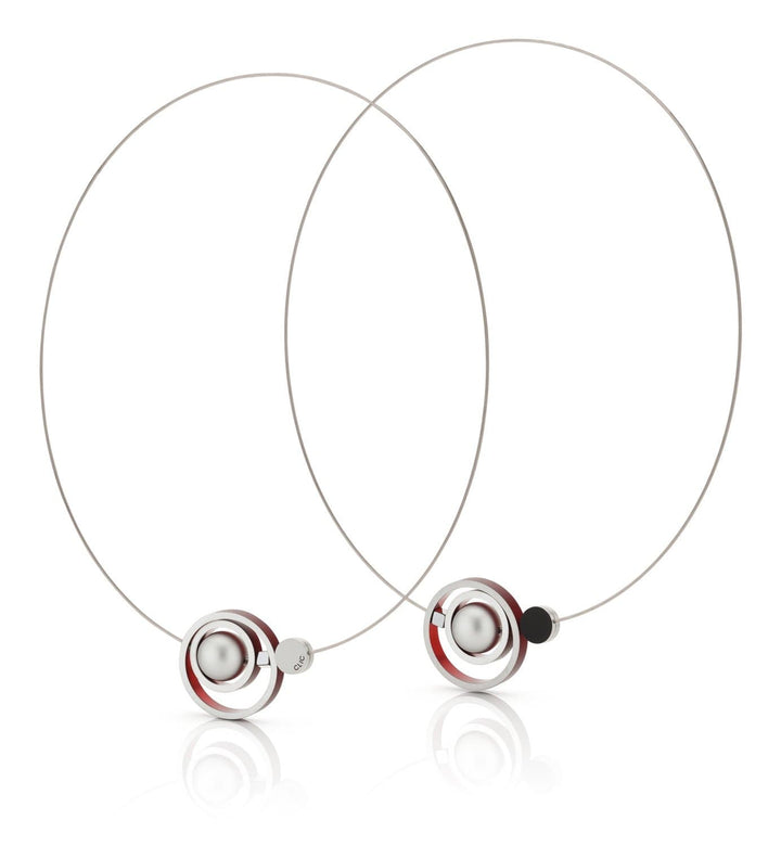 De Collier Ringen in elkaar Rood C187R van CLIC Creations zijn minimalistische zilveren creolen met een centrale metalen bol, omringd door rode en zwarte ringen. Handgemaakt in Nederland, ze bieden een modern, geometrisch ontwerp met reflecterende oppervlakken.