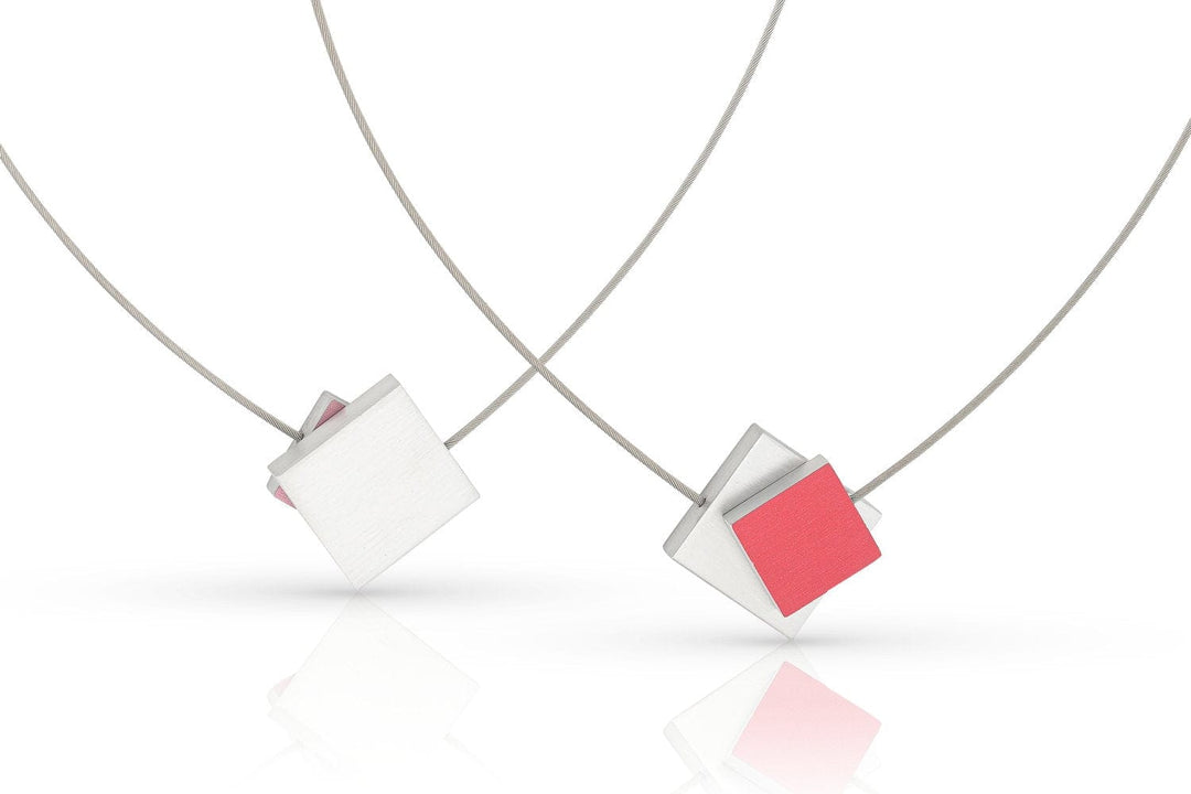 Het Collier Vierkant met gekleurd vierkant C263R van CLIC Creations bestaat uit twee minimalistische kettingen met vierkante hangers, elk met gelaagde geometrische vormen - één in geborsteld metaal en één in opvallend roze - opgehangen aan dunne draadkettingen tegen een witte achtergrond.