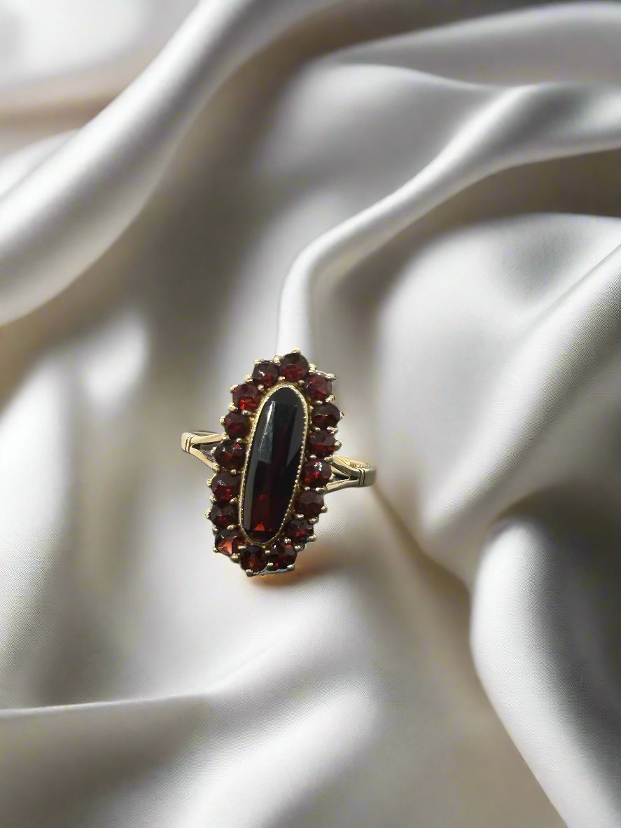 Anello vintage in oro 14k con granato ovale centrale e pietre granato circondanti.
