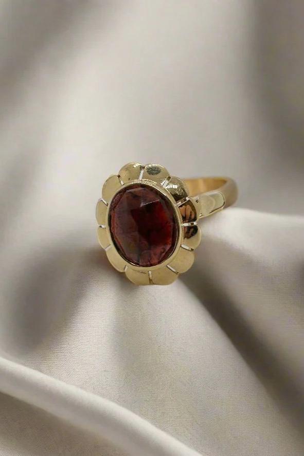 De Vintage Collectie van Juwelier van der Kooij bestaat uit een vintage gouden ring van 14 karaat goud, met een gewicht van 3,5 gram, met een elegante bloemenzetting waarin een grote, donkerrode ovale kwarts-edelsteen op lichtgekleurde stof is gezet voor een verfijnde uitstraling.