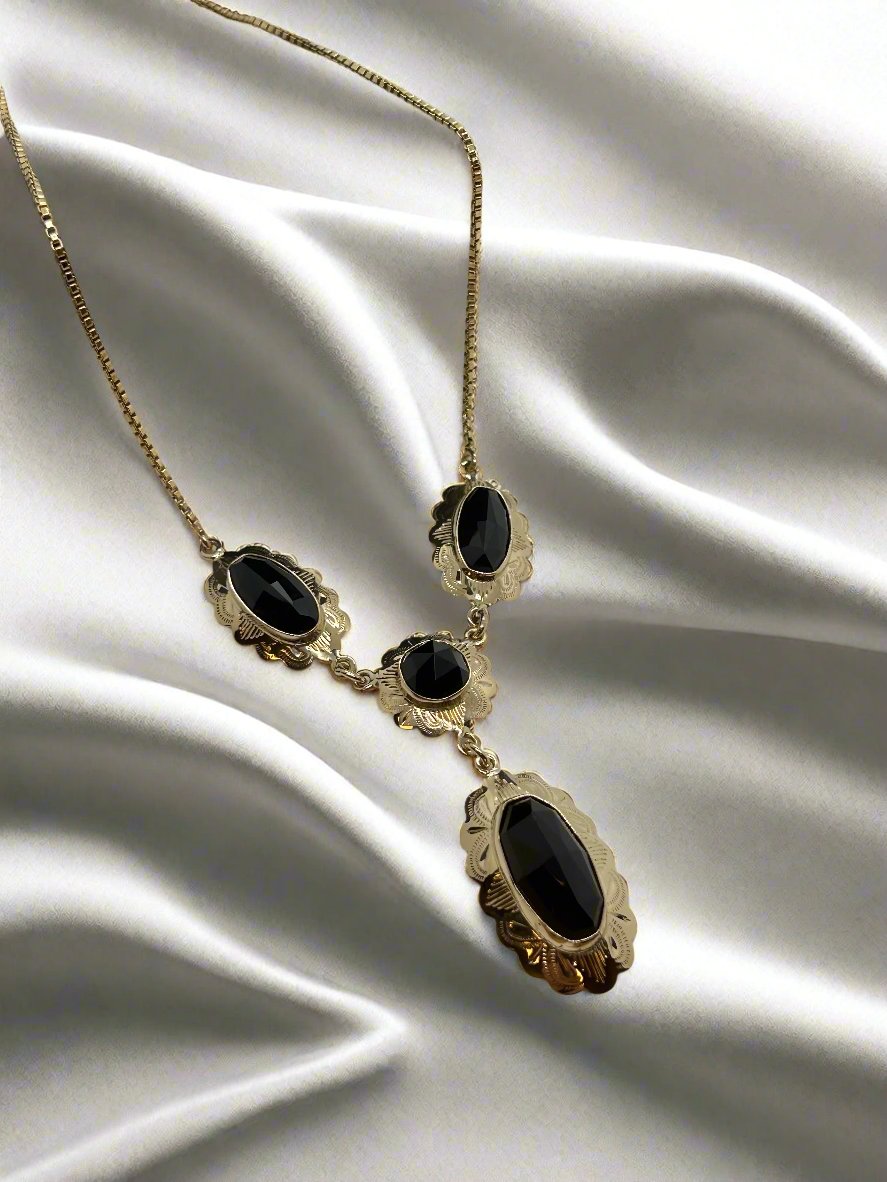 Het vintage gouden collier 14K Venetiaans met granaat (9,6 gram) van Juwelier van der Kooij, versierd met vier zwarte ovale stenen in gegolfde gouden lijstjes, rust elegant op gladde, witte satijnen stof.
