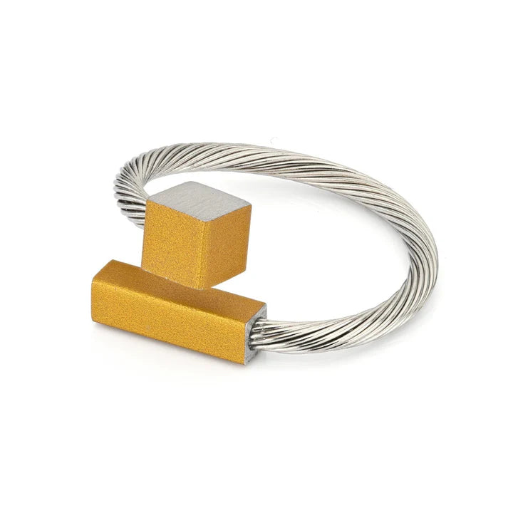 Anello con barretta gialla e cubo argentato su una base di filo metallico.