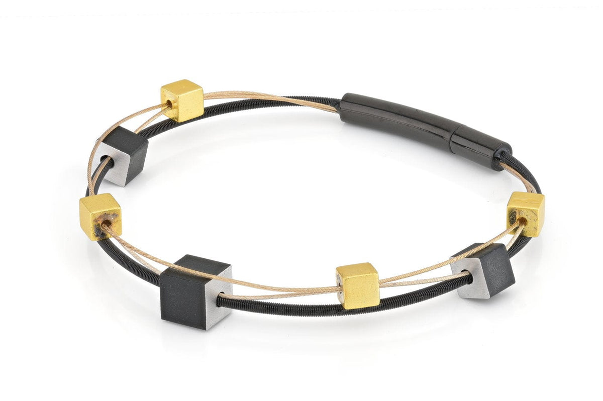 Bracciale con cubetti giocosi in oro e nero, con dettagli in metallo e corda elastica.