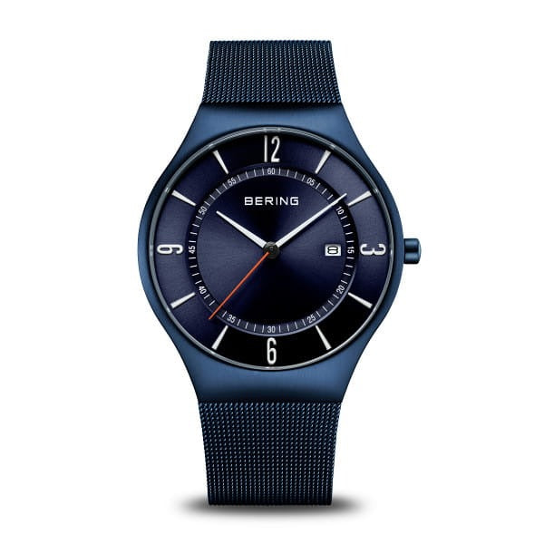 Orologio con cassa blu, quadrante blu scuro, cinturino in maglia e dettagli bianchi.