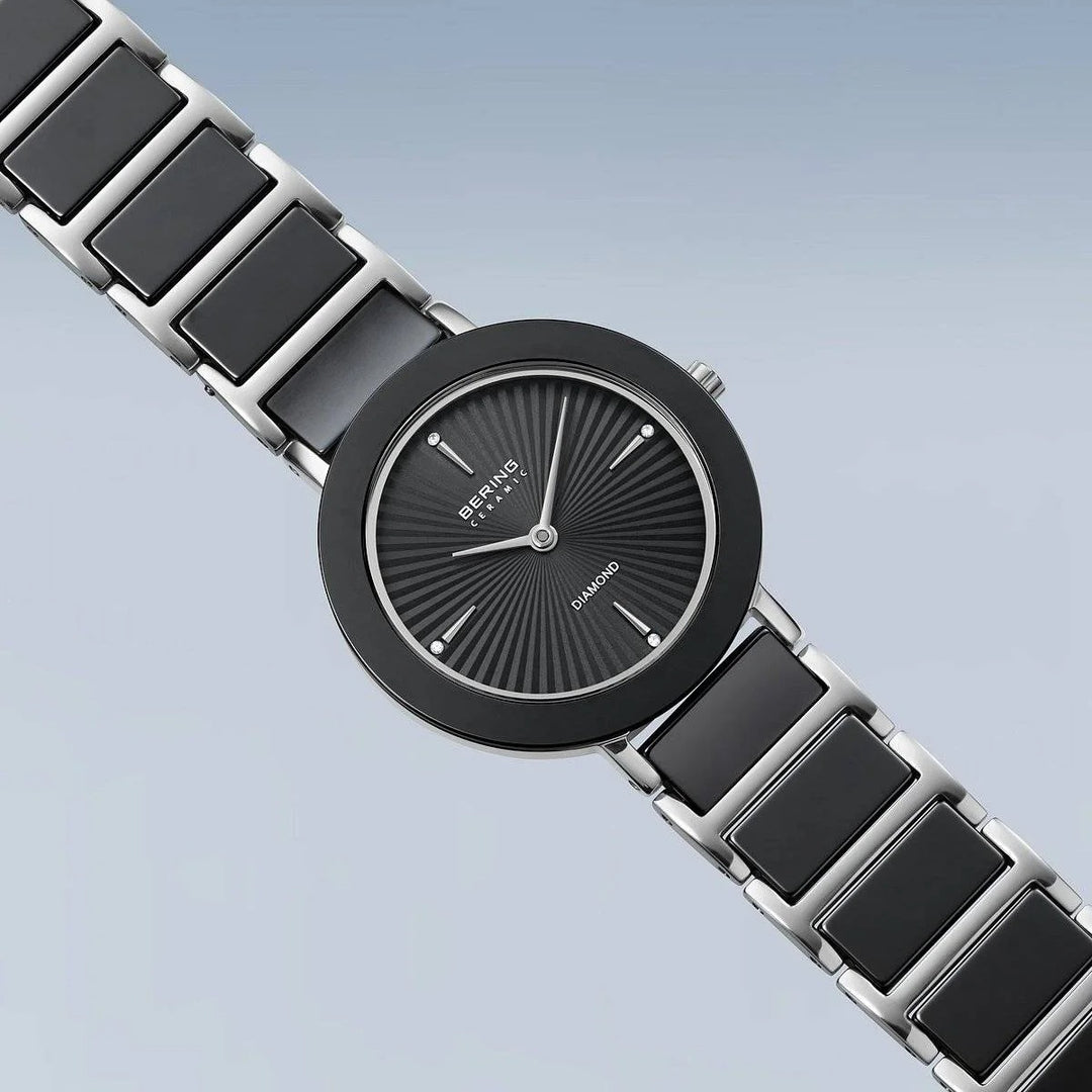 Het Bering dames horloge 11429-702 heeft een moderne zwarte en zilveren band, ronde zwarte wijzerplaat, minimalistische markers, "Diamond" detail op de wijzerplaat en saffierglas - alles tegen een zacht lichtblauw kleurverloop.
