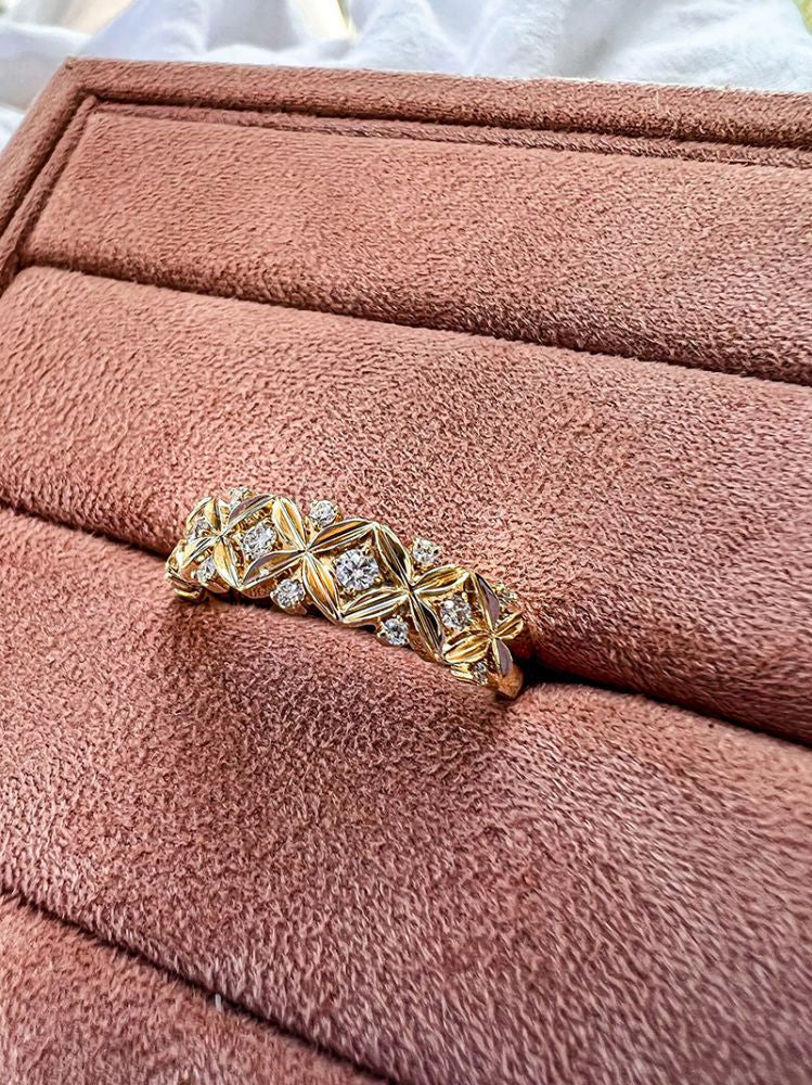 De Verfijnde Geelgouden Ring met Diamant - 0,19 crt van Excellent Jewelry, met een ingewikkeld geometrisch patroon en kleine diamantjes, wordt gepresenteerd op een zacht, roze fluwelen sieradenplateau.