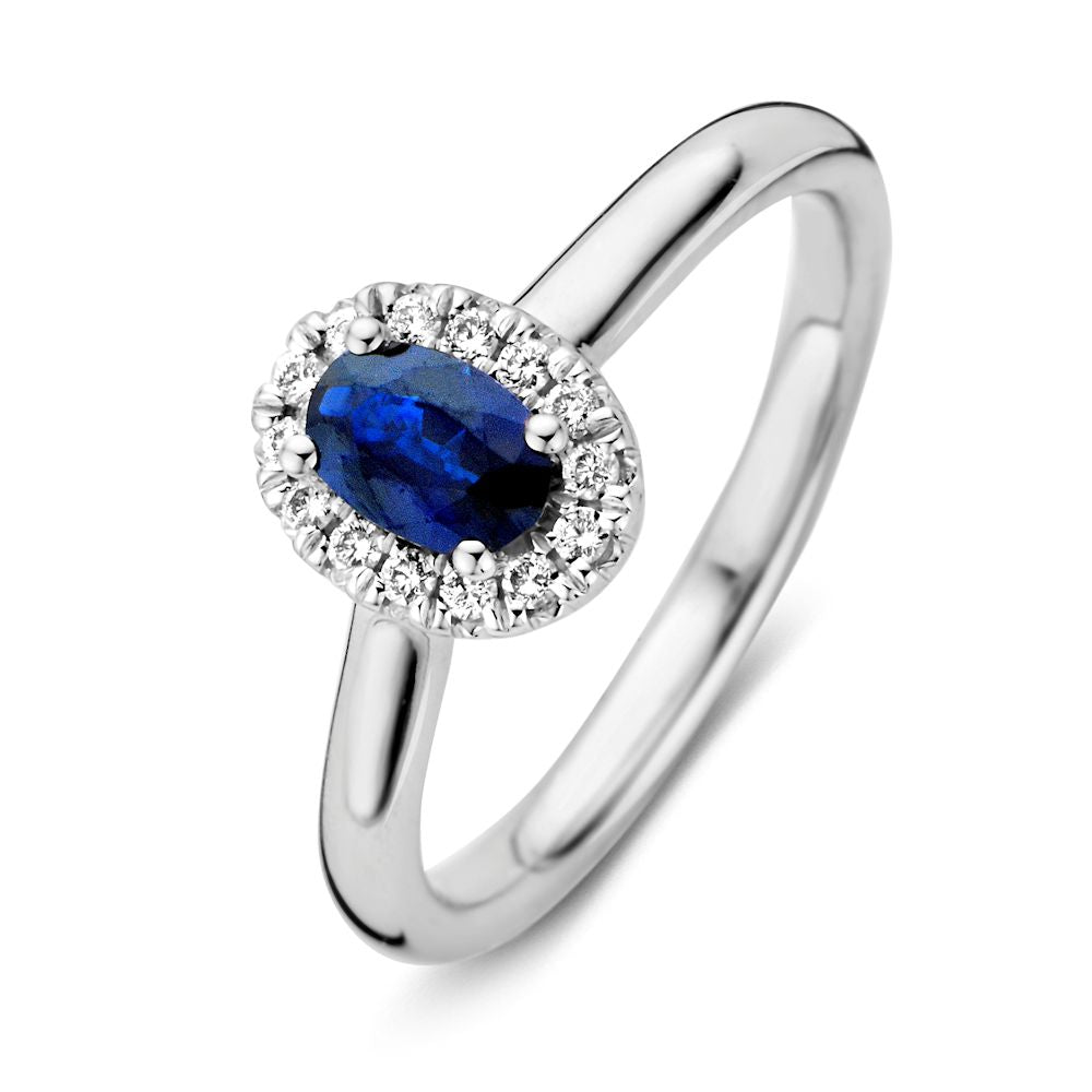 Anello in oro bianco con zaffiro blu ovale e diamanti circondati.