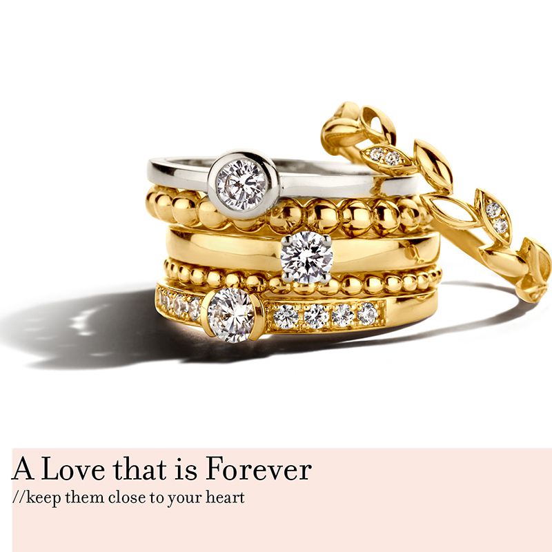 Een stapel gouden en diamanten ringen, waaronder de Excellent Jewelry Witgouden Solitair Ring met Zirkonia - Perfect voor Aanschuifringen, gerangschikt op een wit vlak. Tekst onder: A Love that is Forever // hou ze dicht bij je hart.