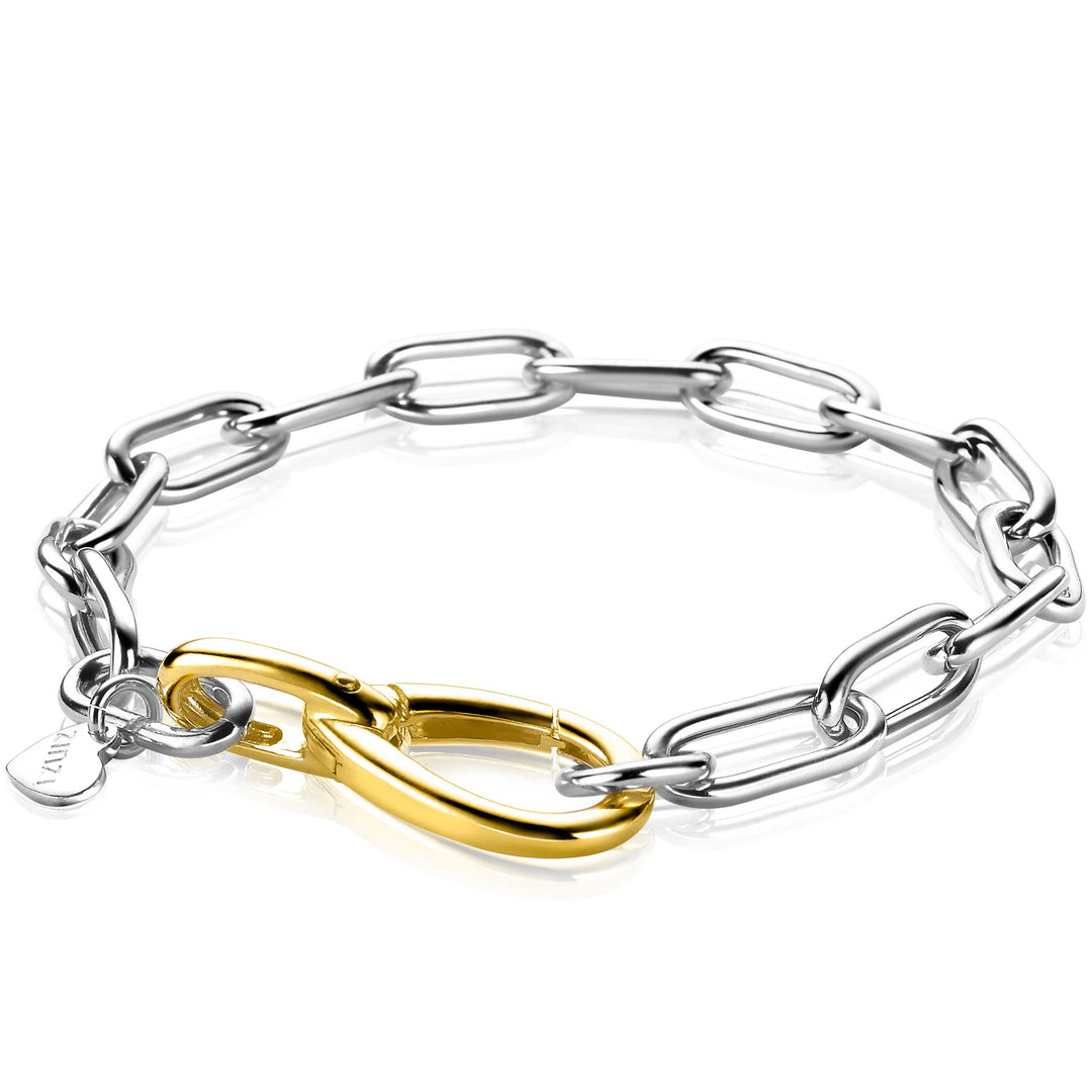 De Zinzi Armband Gold Plated Zia2106 toont grote, in elkaar grijpende schakels als een paperclipketting met een gouden sluiting. Een klein rond label versterkt de elegantie en combineert naadloos minimalistische charme in zilver- en goudtinten.