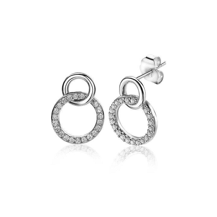 De Zinzi Oorbellen Zilver Zio1782 zijn zilveren oorbellen van Zinzi, met twee in elkaar grijpende open cirkels - één versierd met fonkelende heldere steentjes - op een witte achtergrond.